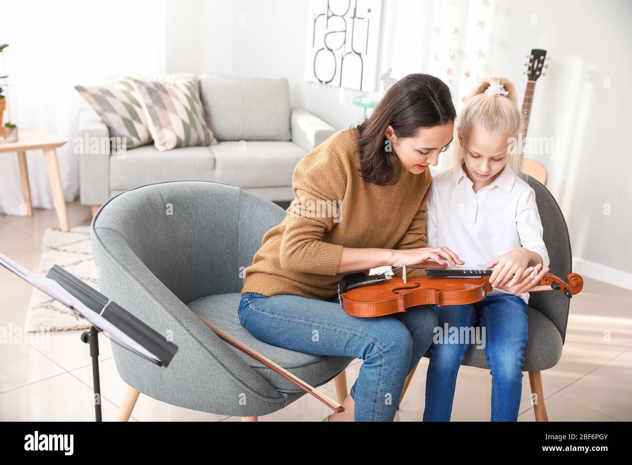 Private music teacher giving violin lessons to little girl at home ...