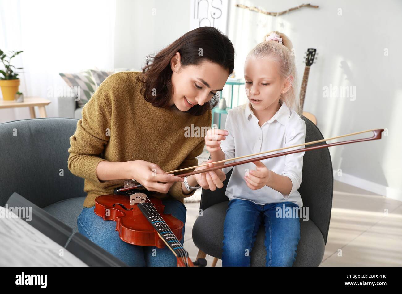 Private music teacher giving violin lessons to little girl at home ...