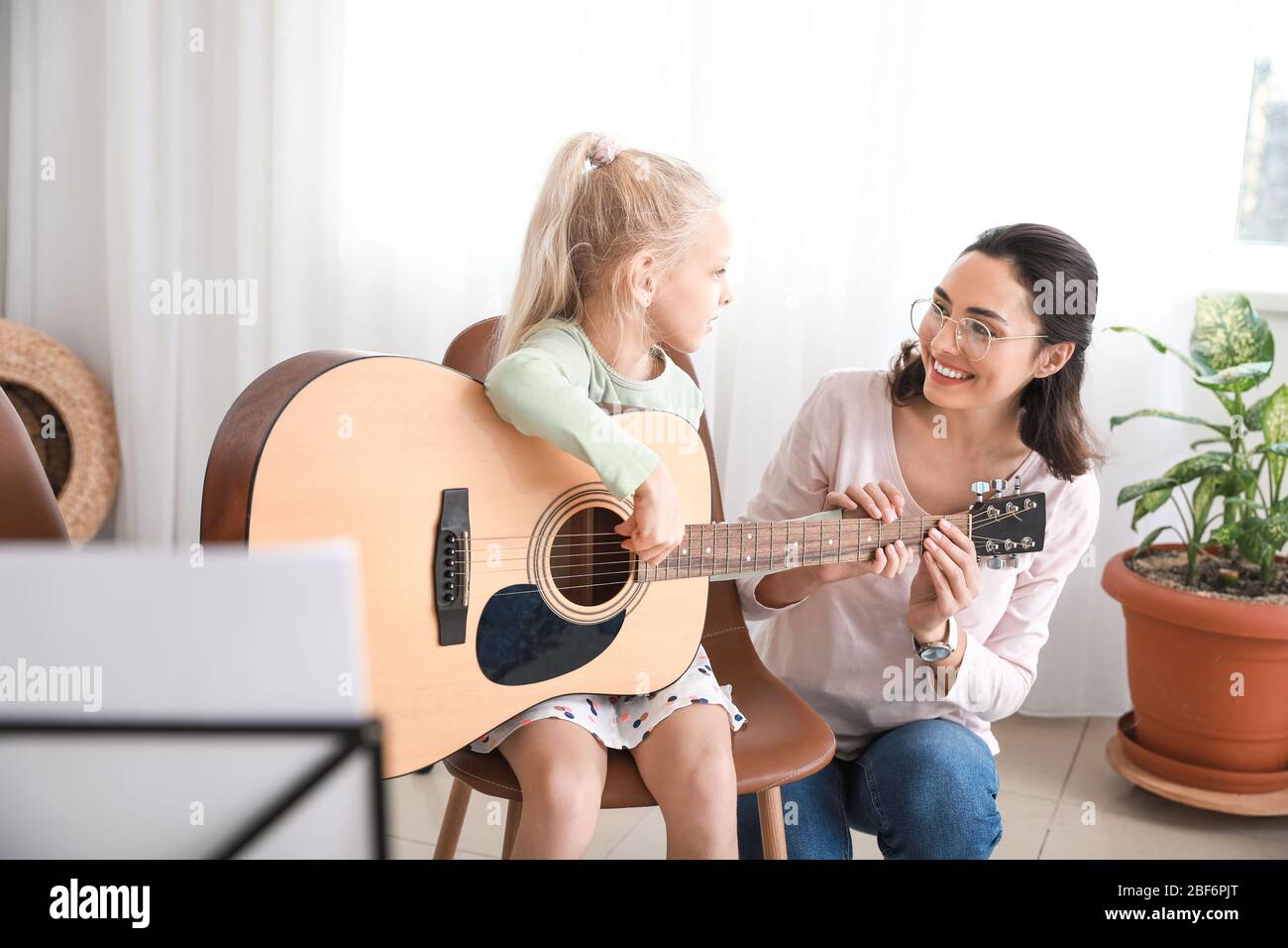 Private music teacher giving guitar lessons to little girl at home ...