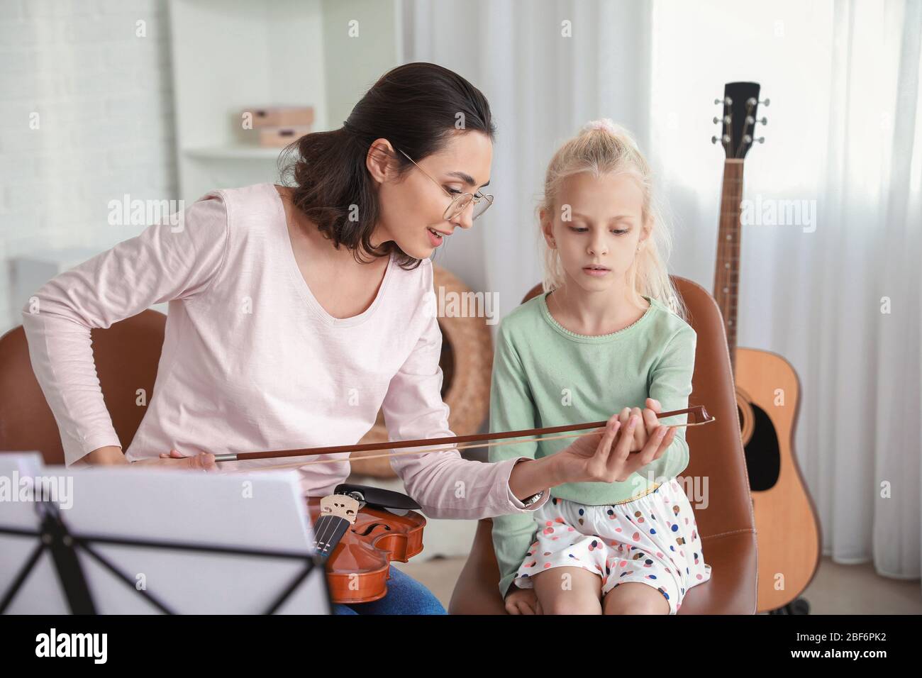 Private music teacher giving violin lessons to little girl at home ...