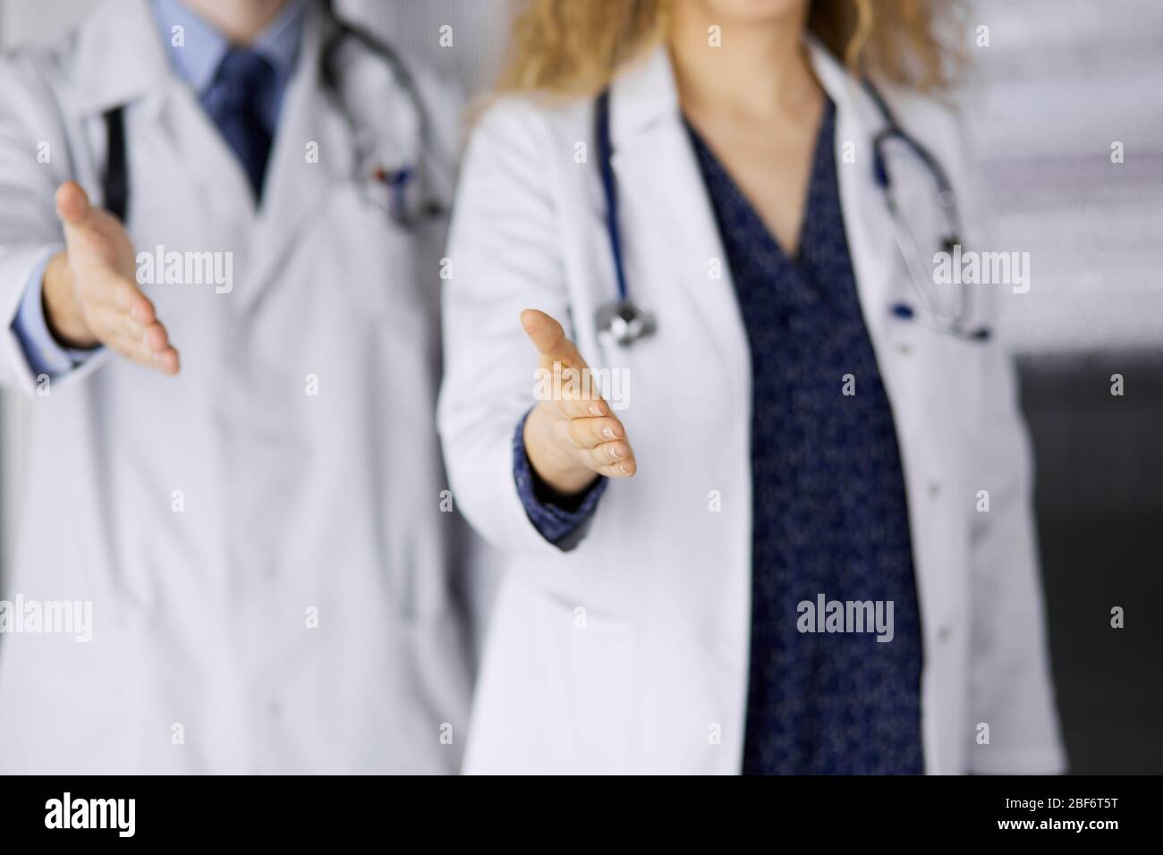 Two doctors standing and offering helping hand for shaking hand or saving life. Medical help, countering viral infection and medicine concept Stock Photo