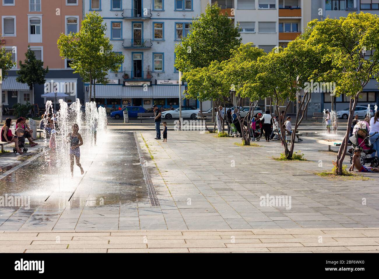 Children play in in water fountain jets with locals relaxing on benches in a public area, Alter Messplatz, Mannheim, Germany. Stock Photo