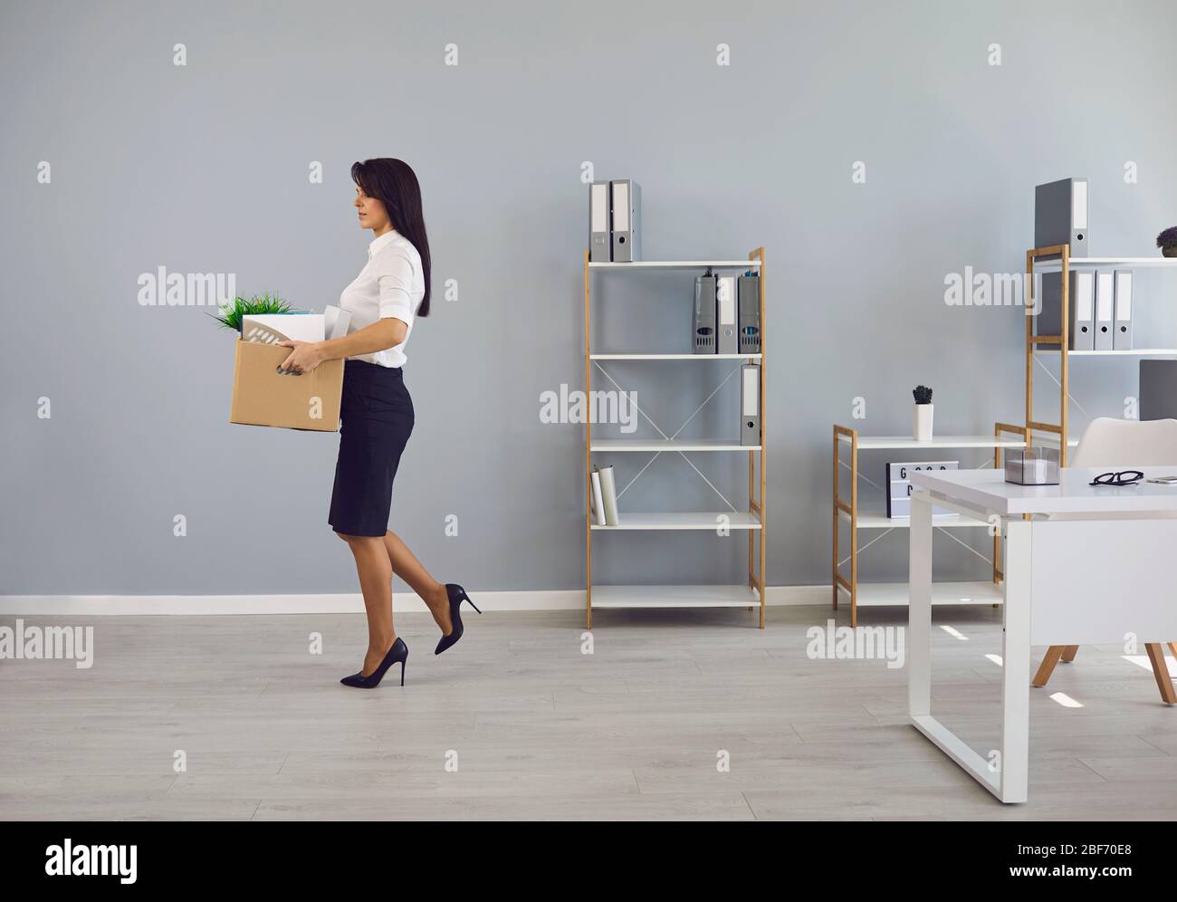 Dismissed unemployed woman worker with a cardboard box in the office leaves in search of a new job. Stock Photo