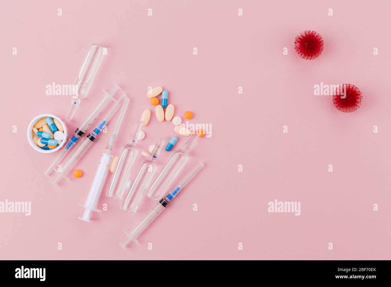 Abstract model of coronavirus infection of the strain Coronavirus. Red virus, syringe and ampoules with medicine, a jar of pills on a pink background, poses a pandemic hazard. Stock Photo