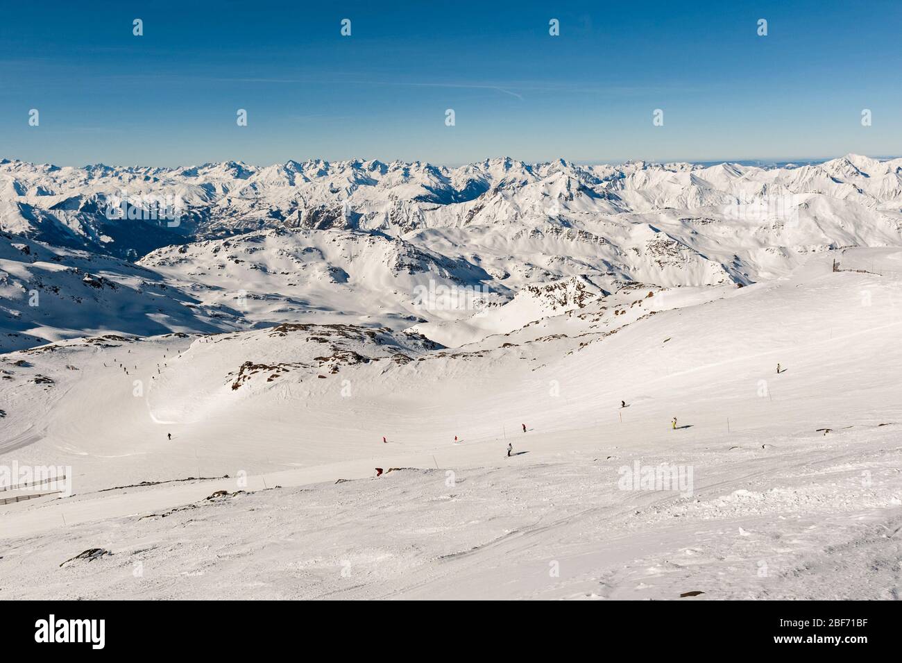 View down an alpine winter sport piste with skiers on mountain in ski resort Stock Photo