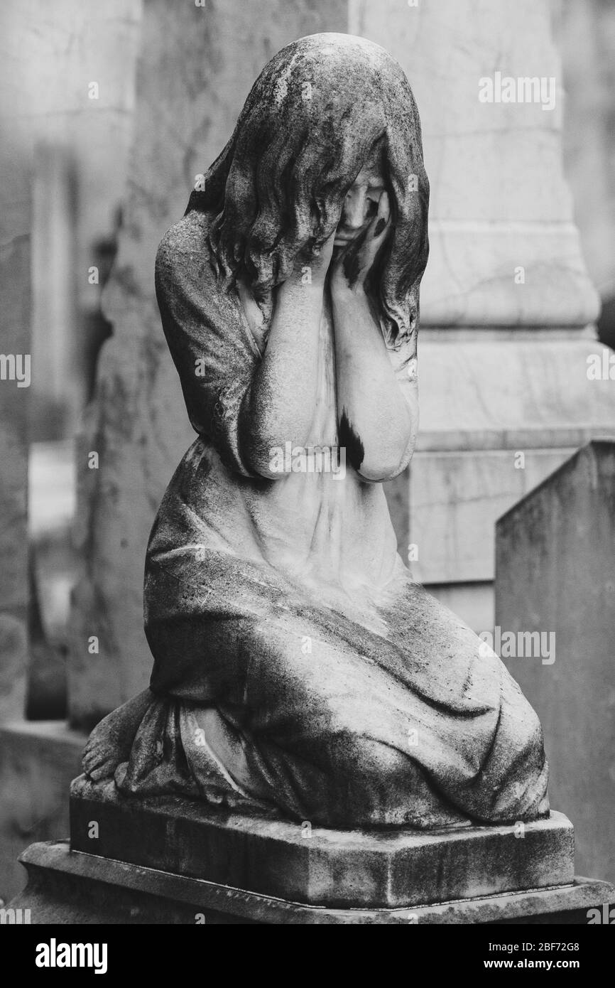 black and white sculpture of a angel girl in an old cemetery. Closeup of stoned angel with closed eyes and cross monument at cemetery. Graveyard old w Stock Photo