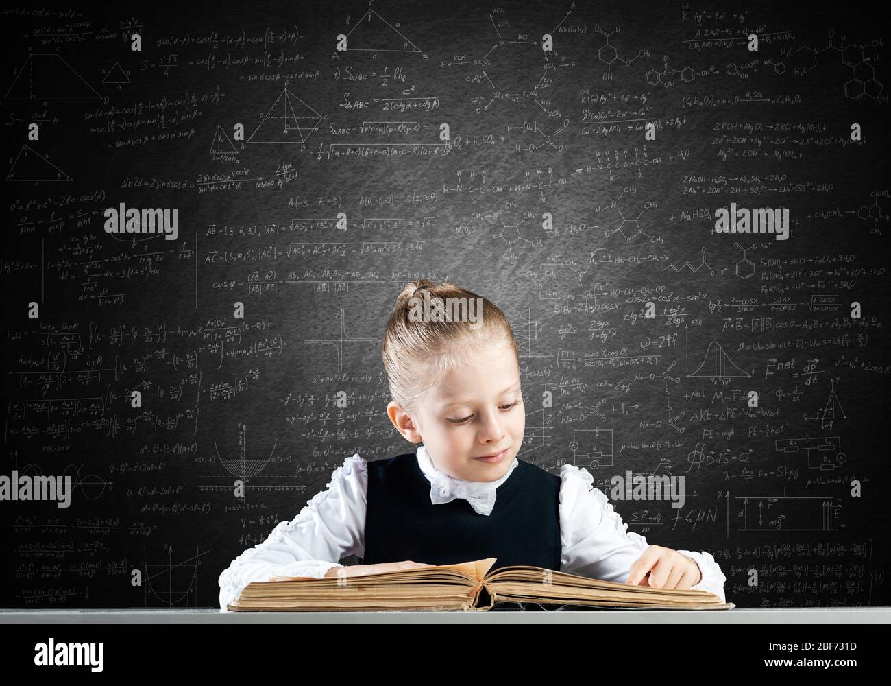 Smiling little girl sitting at desk with open book Stock Photo - Alamy