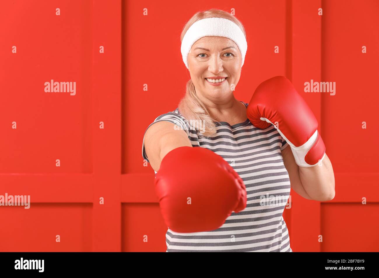 Sporty mature woman in boxing gloves on color background Stock Photo ...