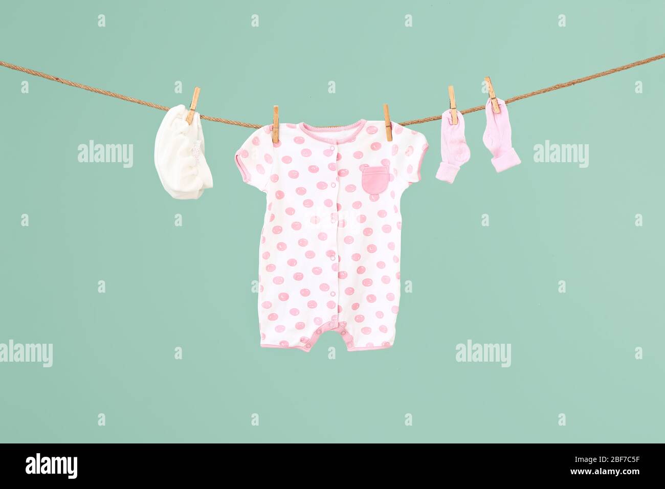 Baby clothes hanging on rope against color background Stock Photo - Alamy