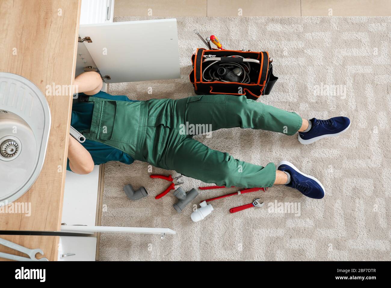 Handsome plumber repairing sink in kitchen Stock Photo