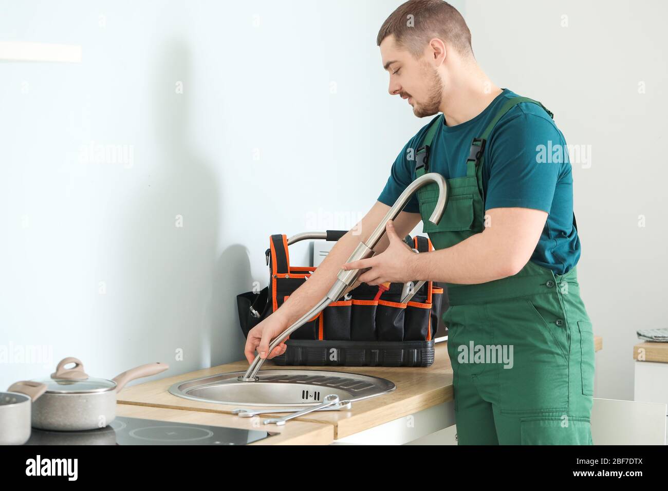Handsome plumber repairing sink in kitchen Stock Photo