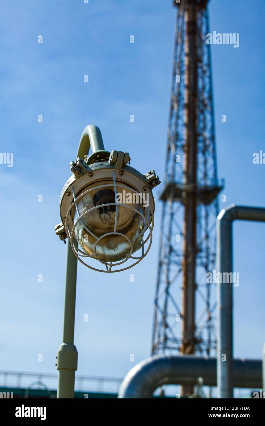 Petrochemical plant. Explosion-proof lamp on oil refinery plant. Focus on foreground. The girder tower blurred on background and blue sky. Stock Photo