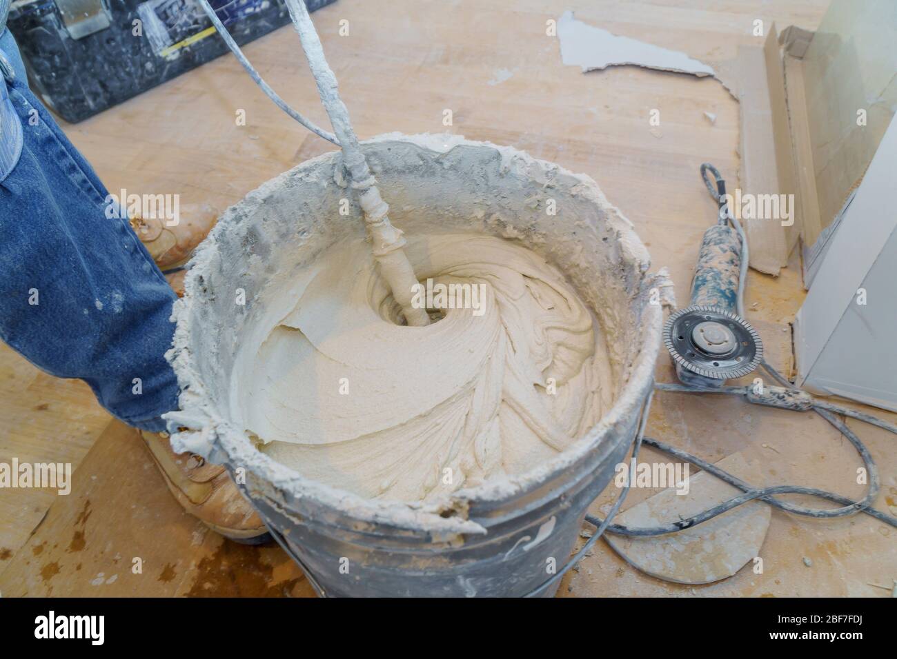 Construction worker mixing tile adhesive or cement with a power drill