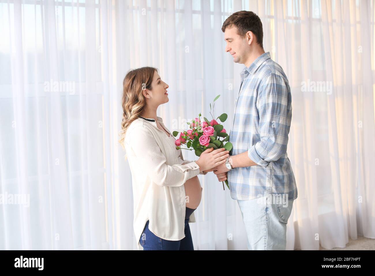 Husband giving bouquet of flowers to his pregnant wife at home Stock