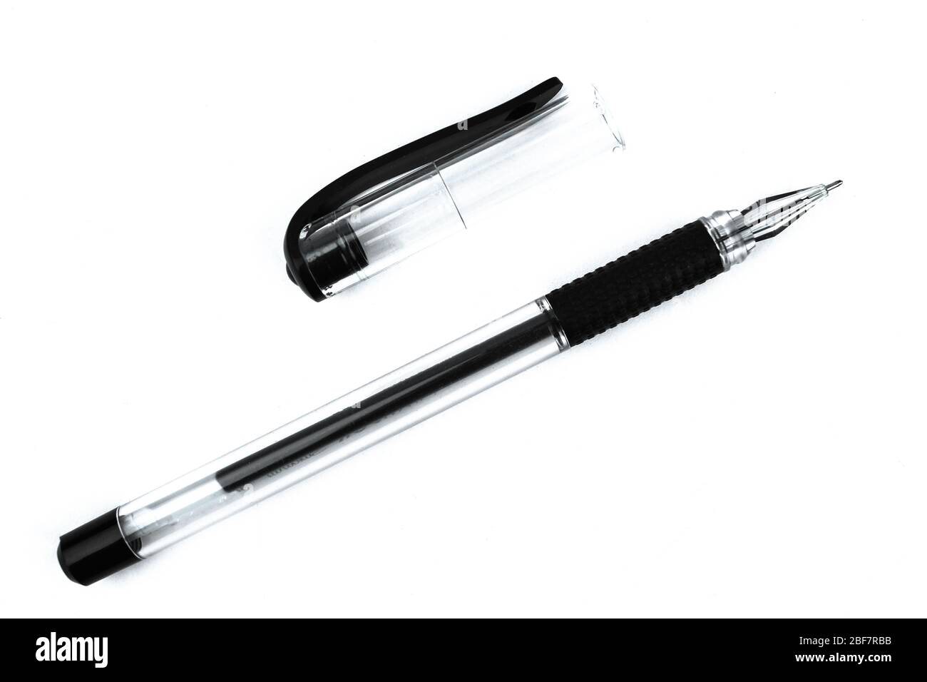 A black colored ball point pen and its cap scattered on top of a white isolated background Stock Photo