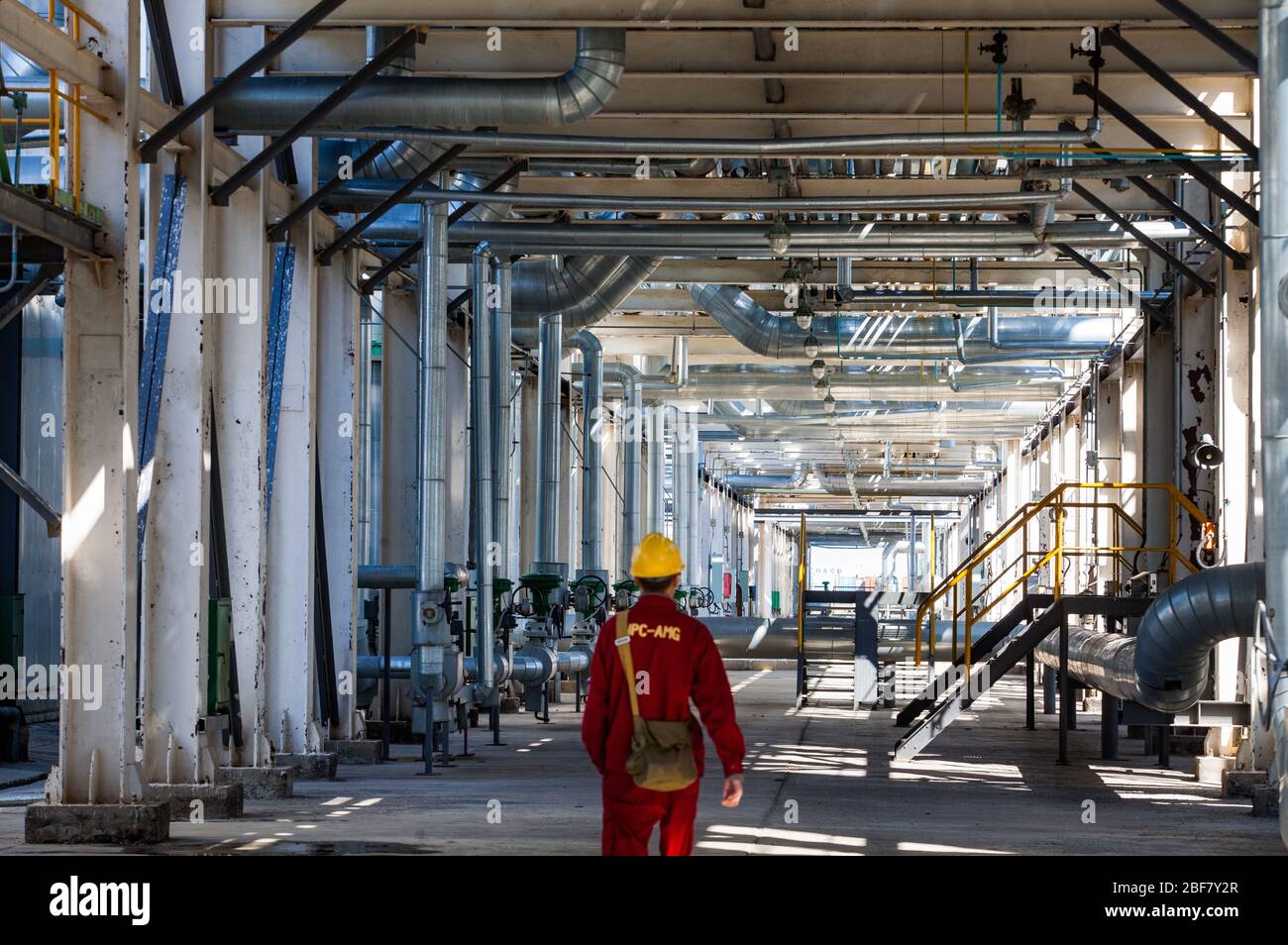 Aktobe region/Kazakhstan - May 04 2012: Refinery worker in red work wear and yellow helmet under the pipelines. Oil refinery plant. CNPC-AMG company. Stock Photo