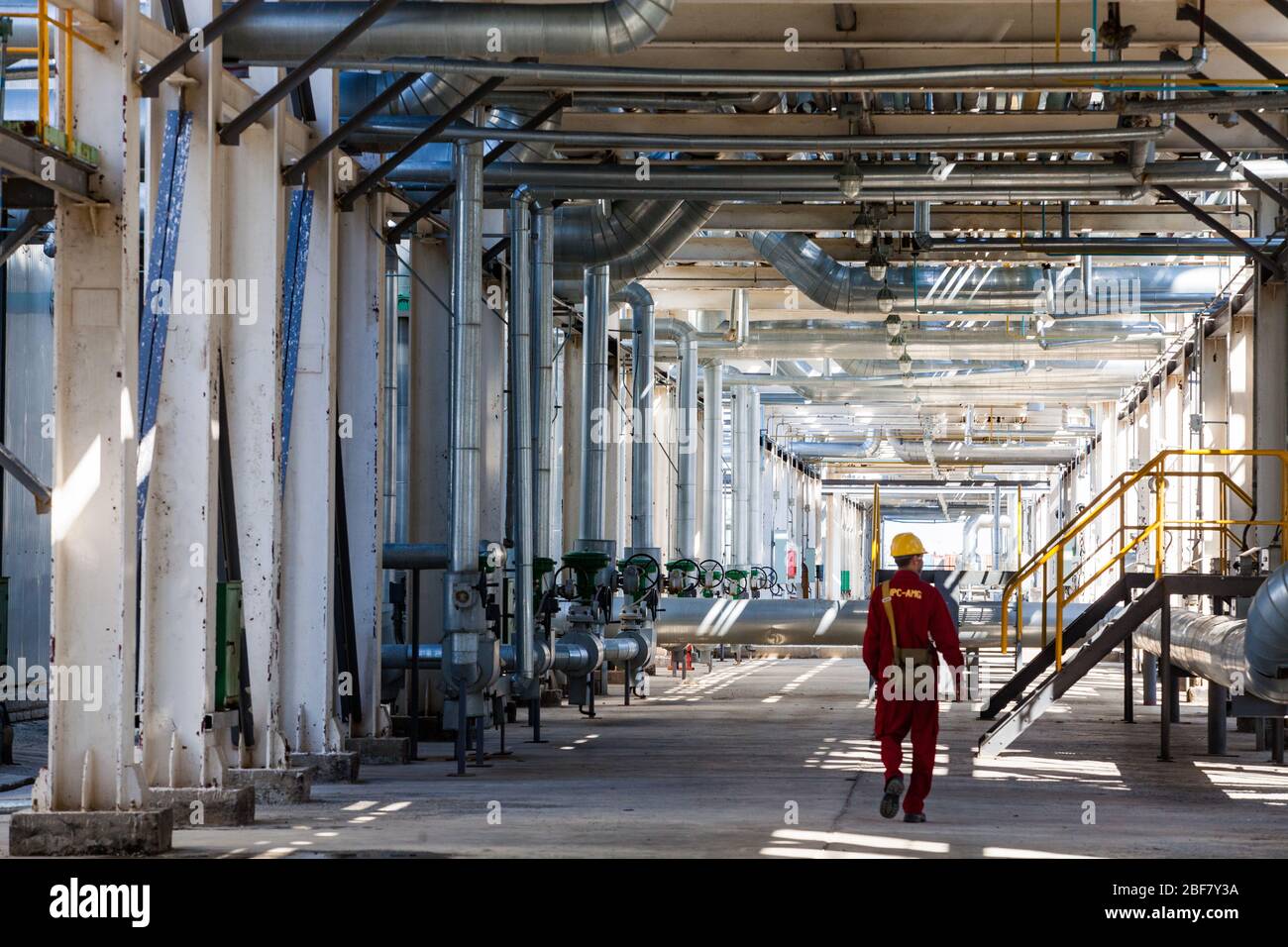 Aktobe region/Kazakhstan - May 04 2012: Refinery worker in red work wear and yellow helmet under the pipelines. Oil refinery plant. CNPC-AMG company. Stock Photo