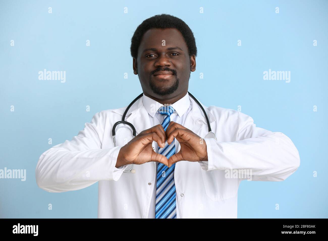 African-American doctor making heart with his hands on color background ...