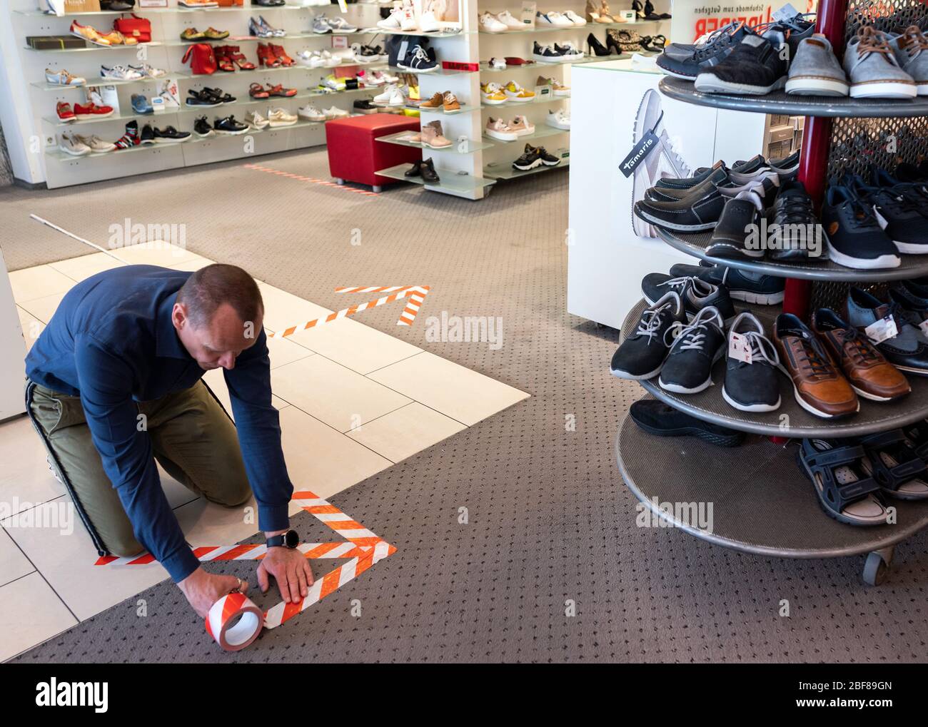 Soest, Germany. 17th Apr, 2020. Owner Marc Schreiber sticks arrows on the  floor at Schuhhaus Schreiber as a guidance system for customers. After the  long break due to the coronavirus pandemic, many