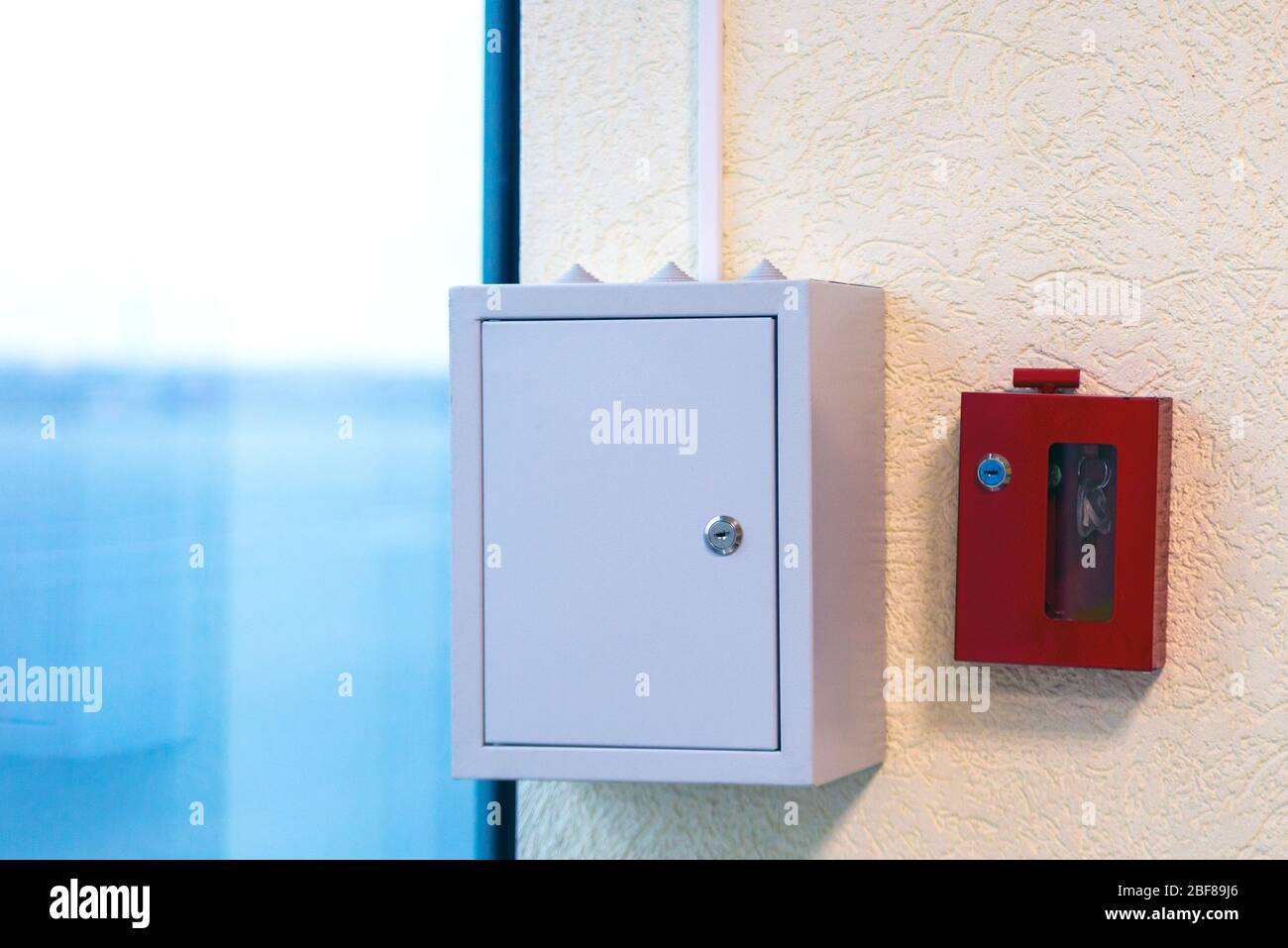 Grey metal box with electrical automatics with and fire alarm and extinguisher equipment in locked key box on wall Stock Photo
