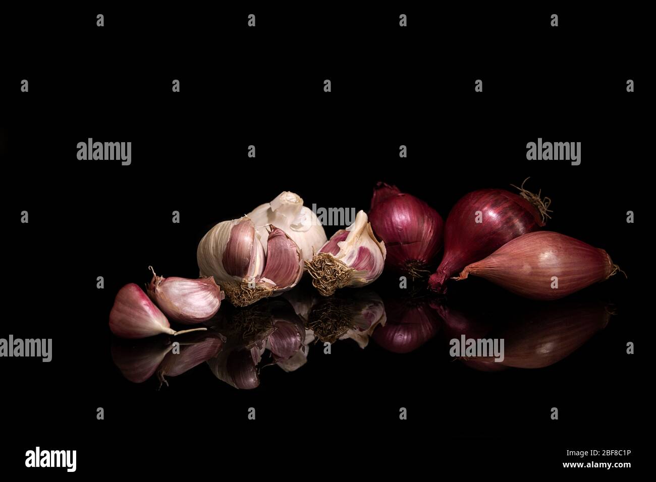 Garlic, red onions and shallot on black background with reflections