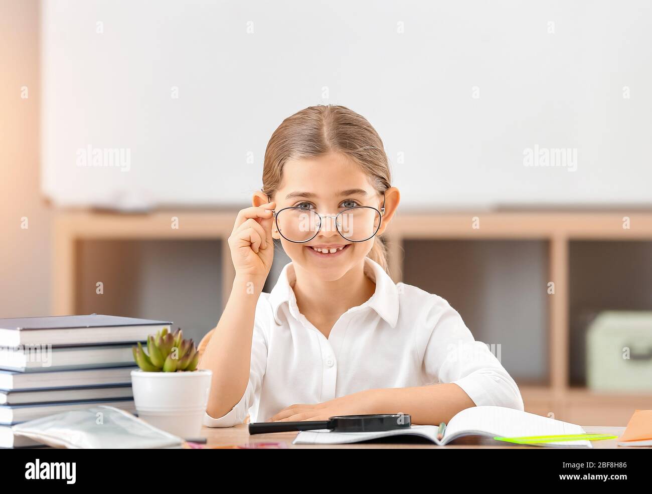 Cute little schoolgirl at desk in classroom Stock Photo - Alamy