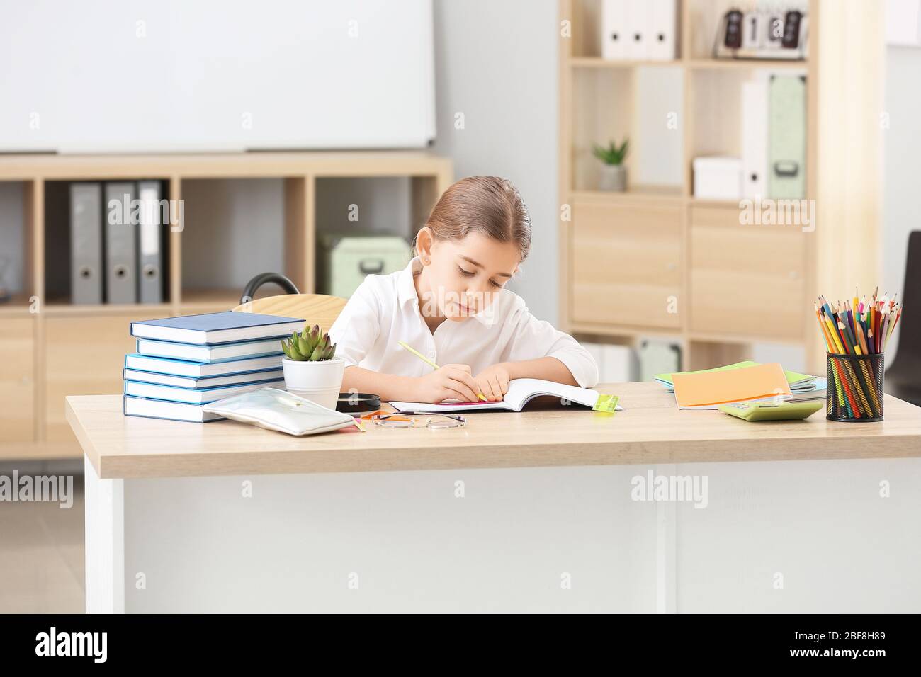 Cute little schoolgirl doing task at desk in classroom Stock Photo - Alamy