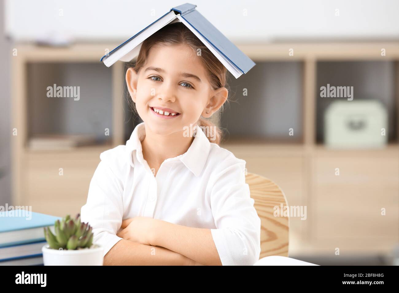 Cute little schoolgirl with book in classroom Stock Photo - Alamy