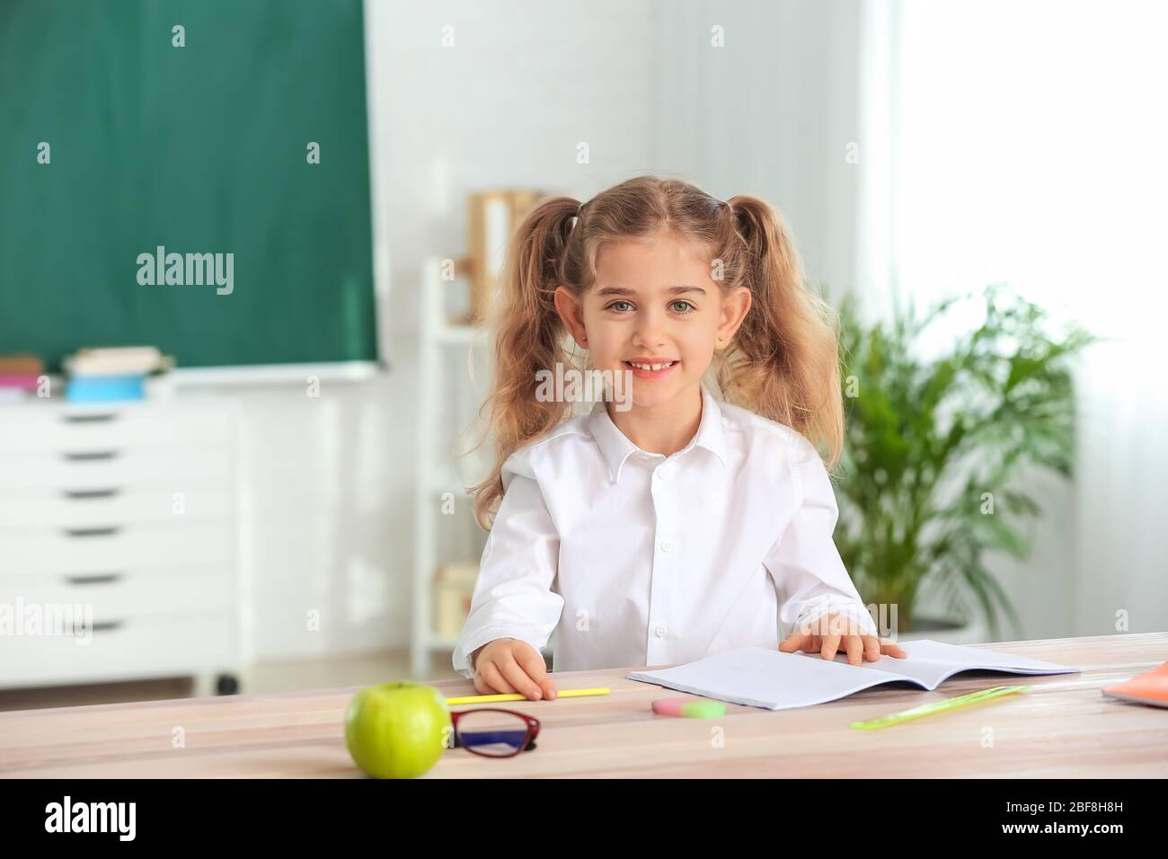 Cute little schoolgirl at desk in classroom Stock Photo - Alamy