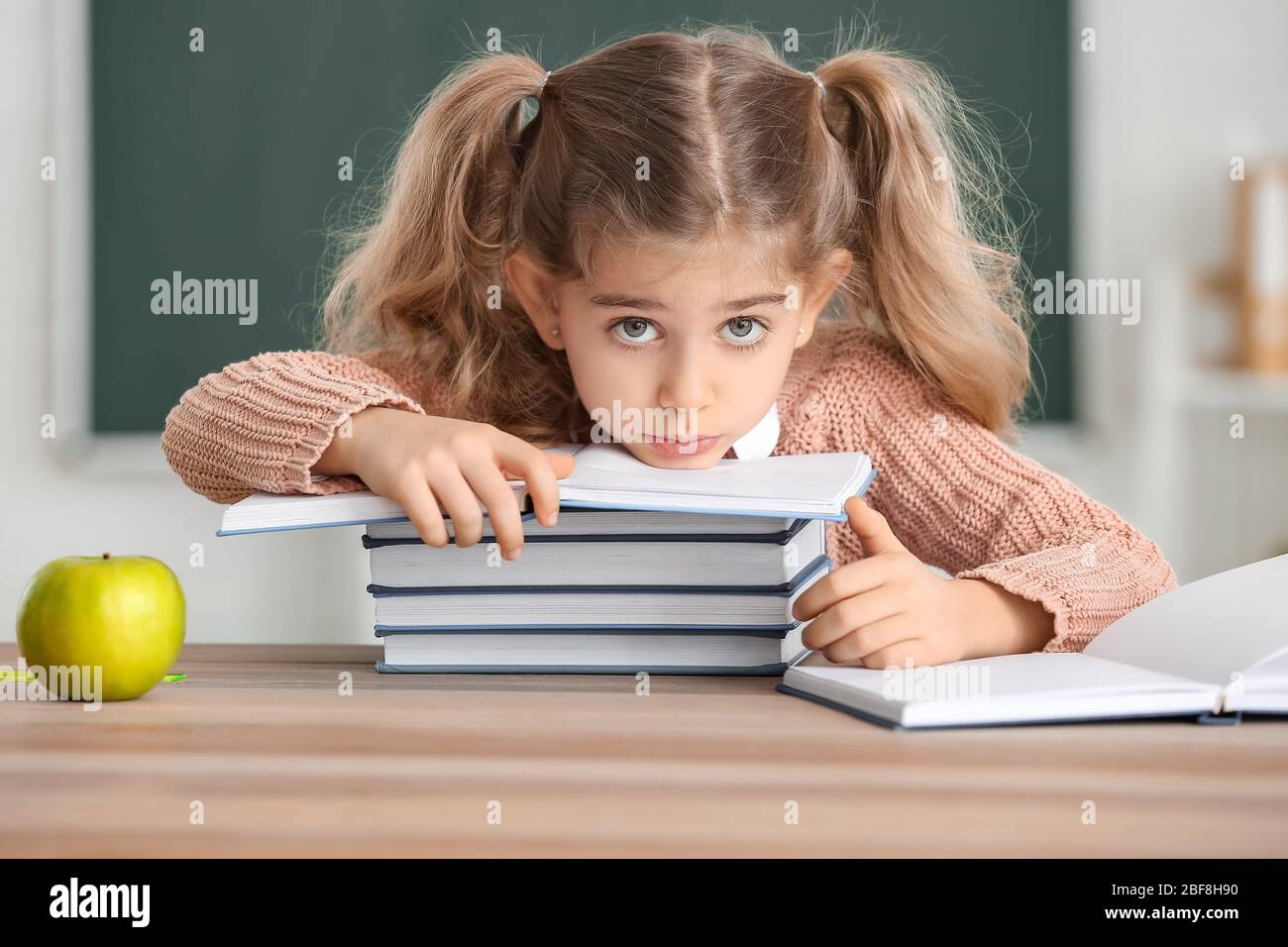 Cute little schoolgirl with books at desk in classroom Stock Photo - Alamy