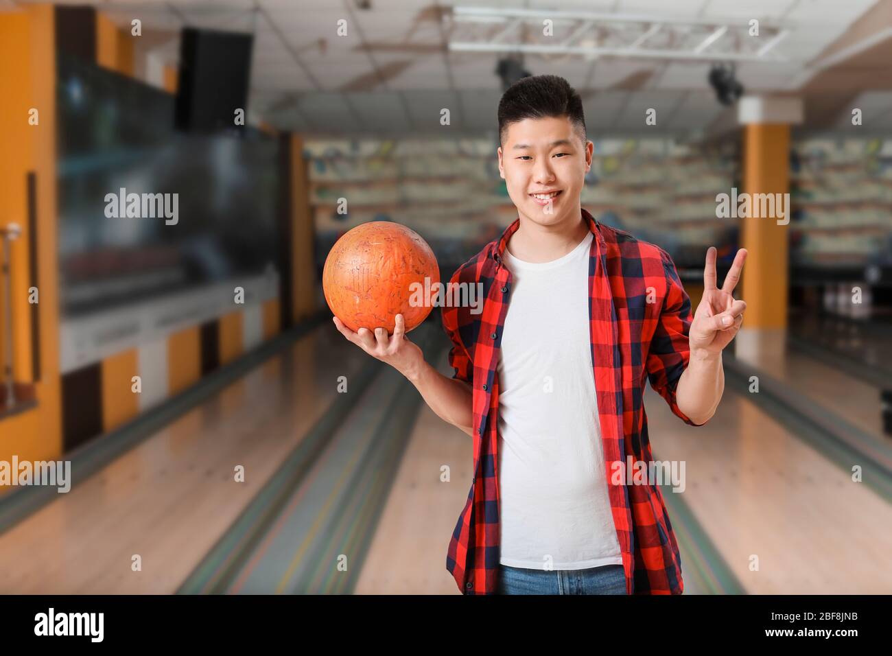 Young Asian man showing victory gesture while playing bowling in club Stock Photo