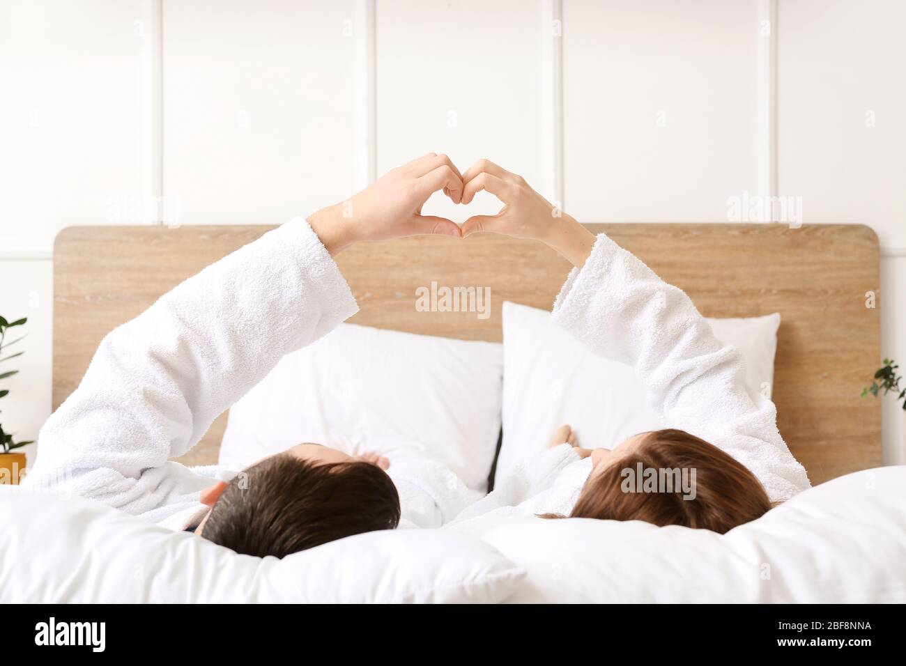 Young couple making heart shape with their hands while lying in bed ...