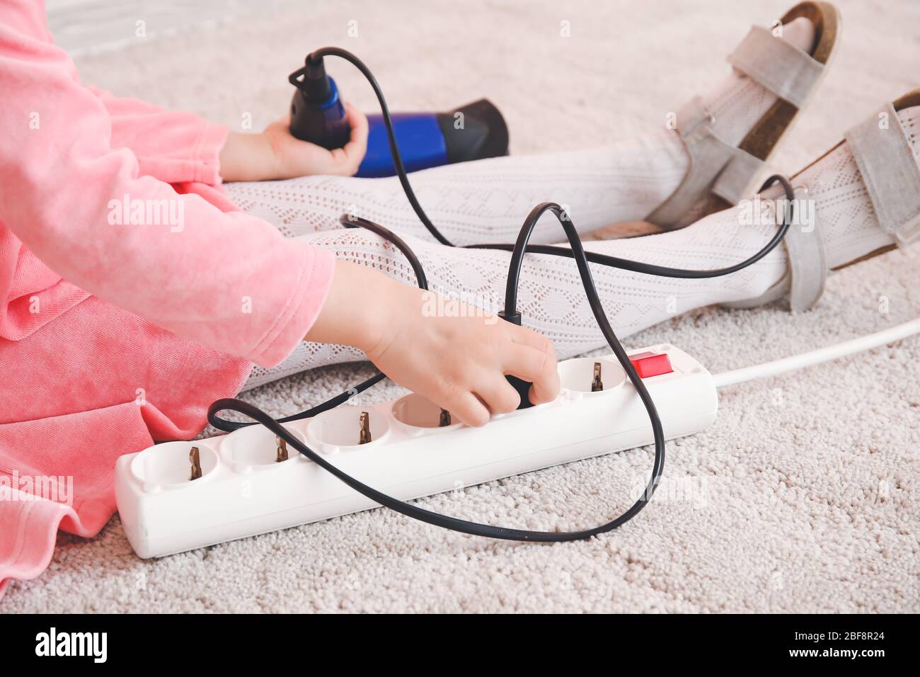 Little girl playing with electric extension cord and blow dryer at home
