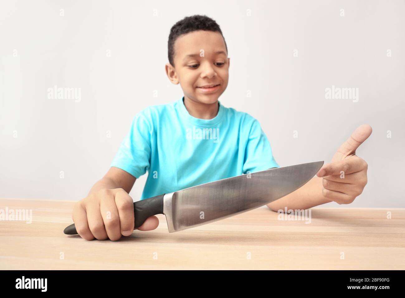 Little AfricanAmerican boy with knife at table. Child in danger Stock
