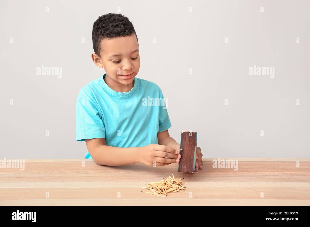 Little African-American boy with matches at table. Child in danger Stock Photo