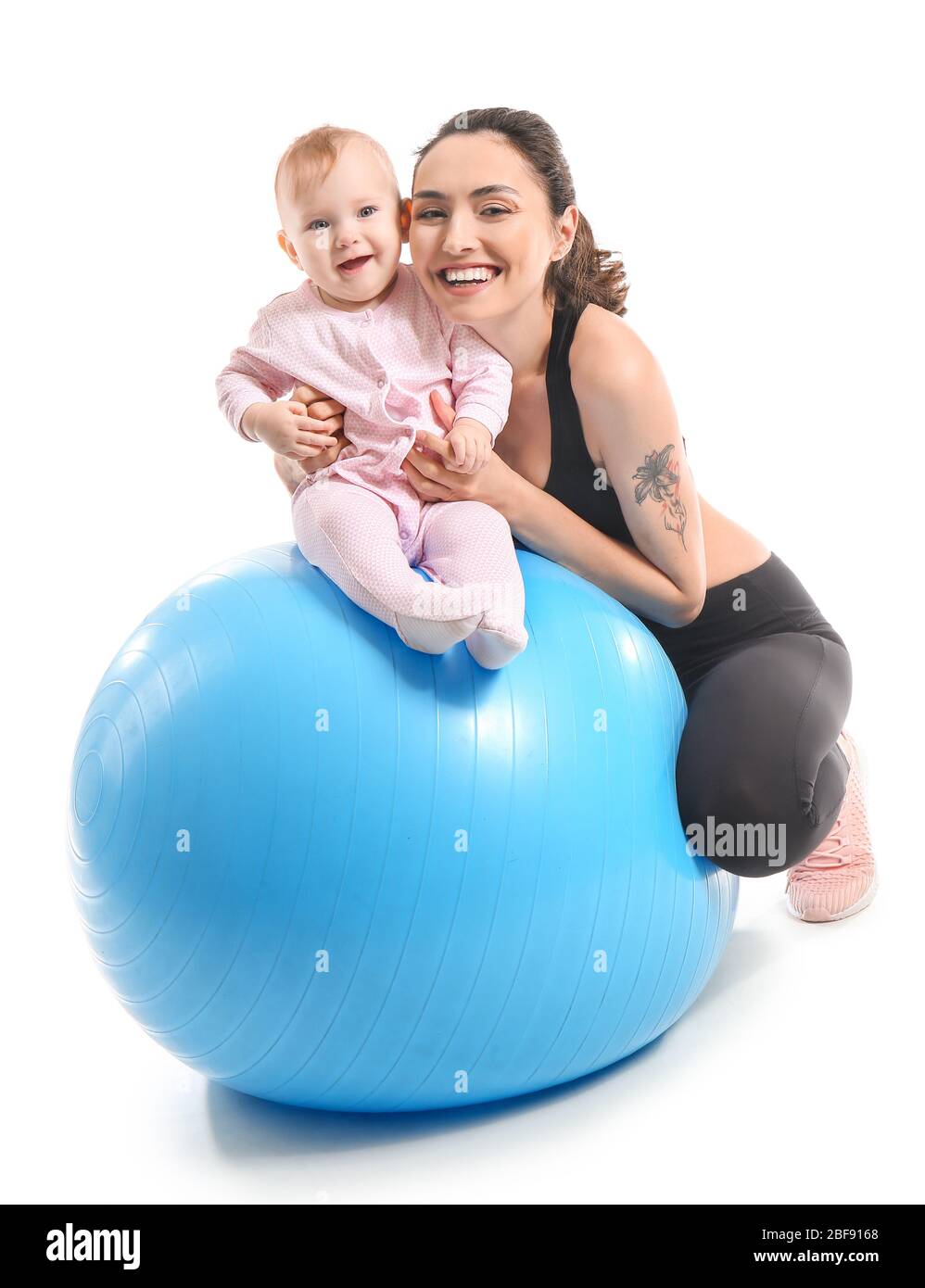 Young sporty mother and her baby doing exercises with fitball on white
