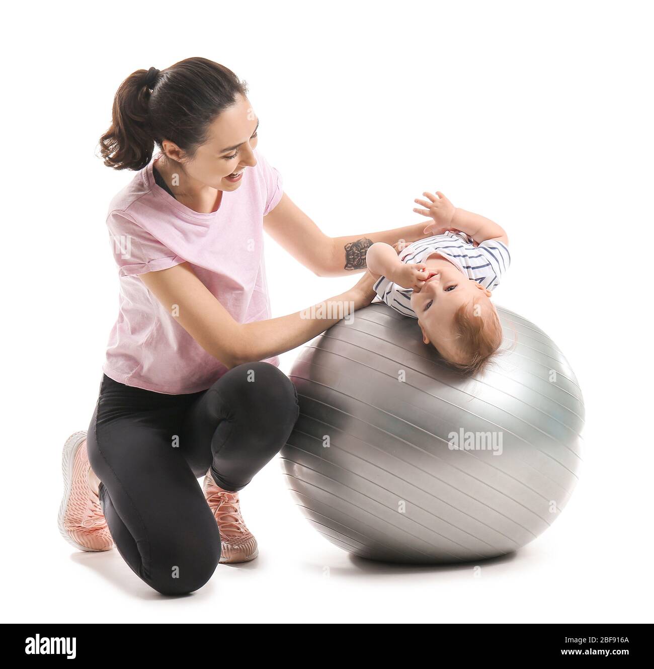 Young sporty mother and her baby doing exercises with fitball on white