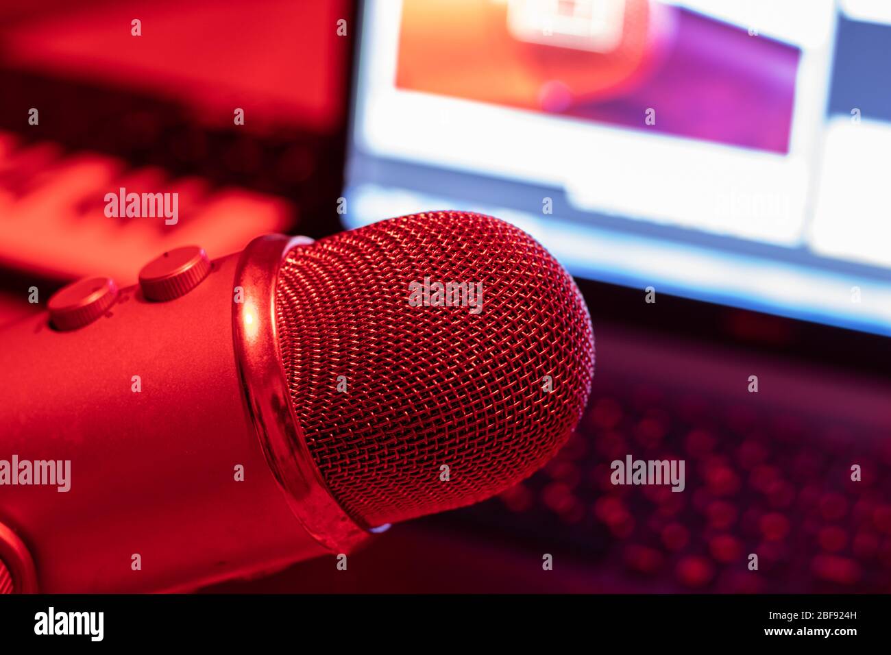 Professional studio condenser microphone on a background of a laptop screen and a music keyboard in red lighting Stock Photo