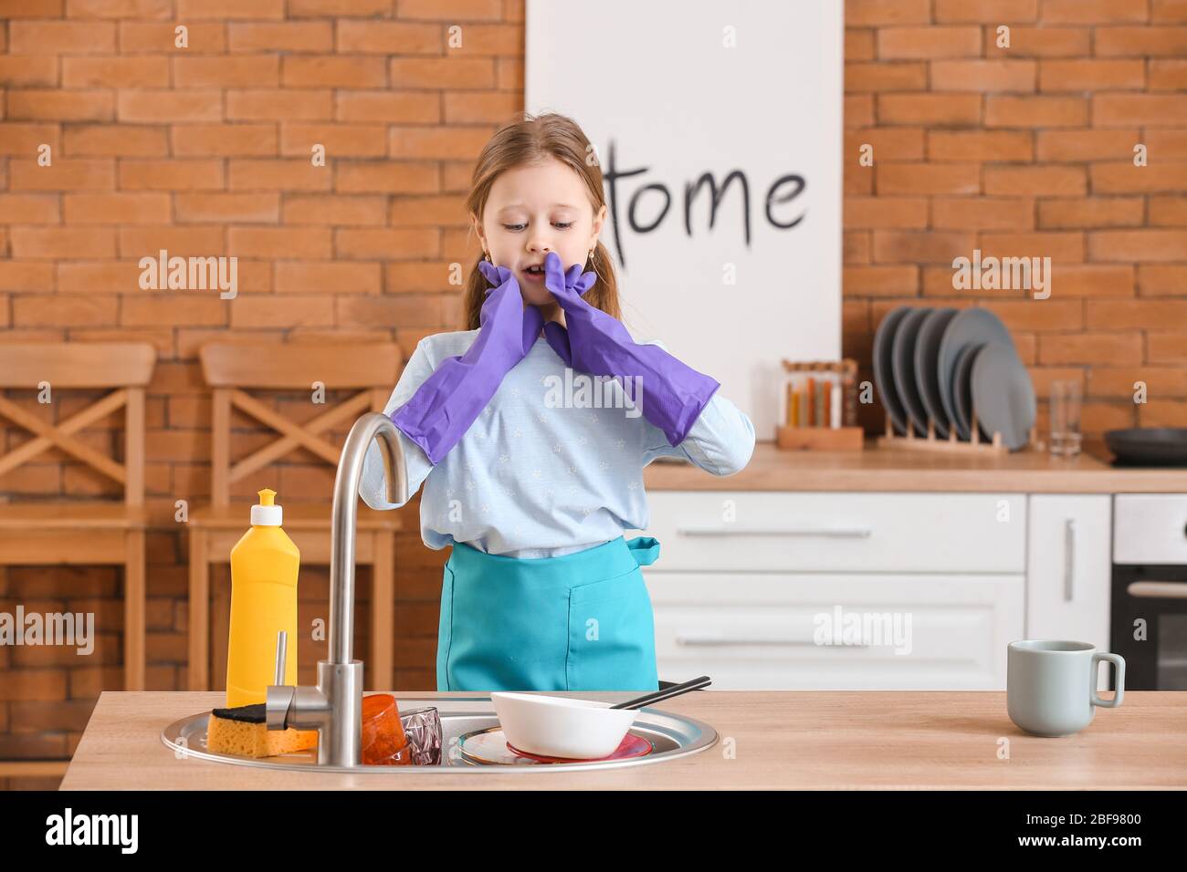Shocked little girl looking at dirty dishes in kitchen sink Stock Photo