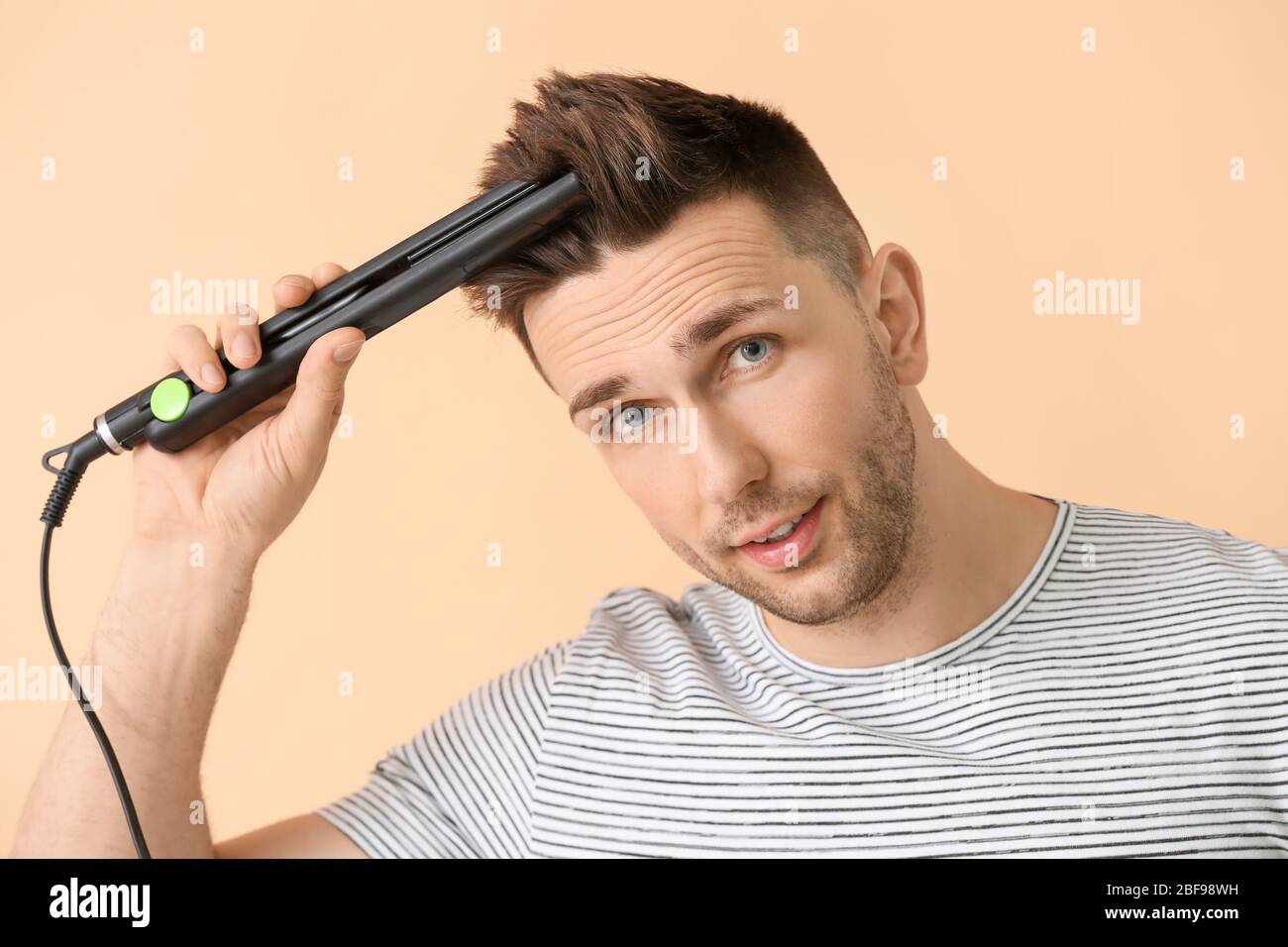 Handsome young man with flattening iron on color background Stock Photo