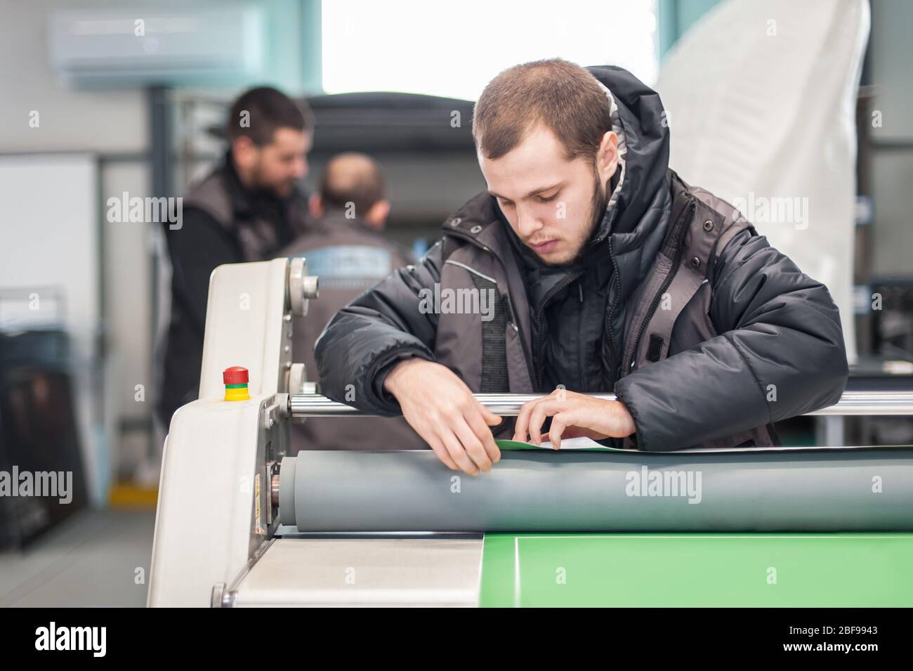 Worker printmaker technician glue large paper poster to foam board with semi automatic gluing machine in digital printshop office Stock Photo