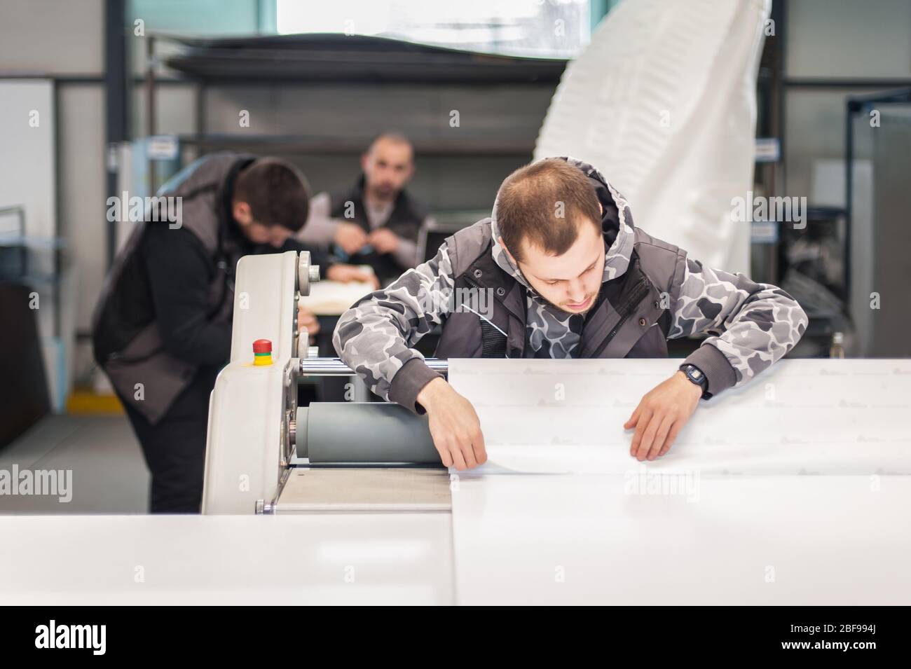 Worker printmaker technician glue large paper poster to foam board with semi automatic gluing machine in digital printshop office Stock Photo