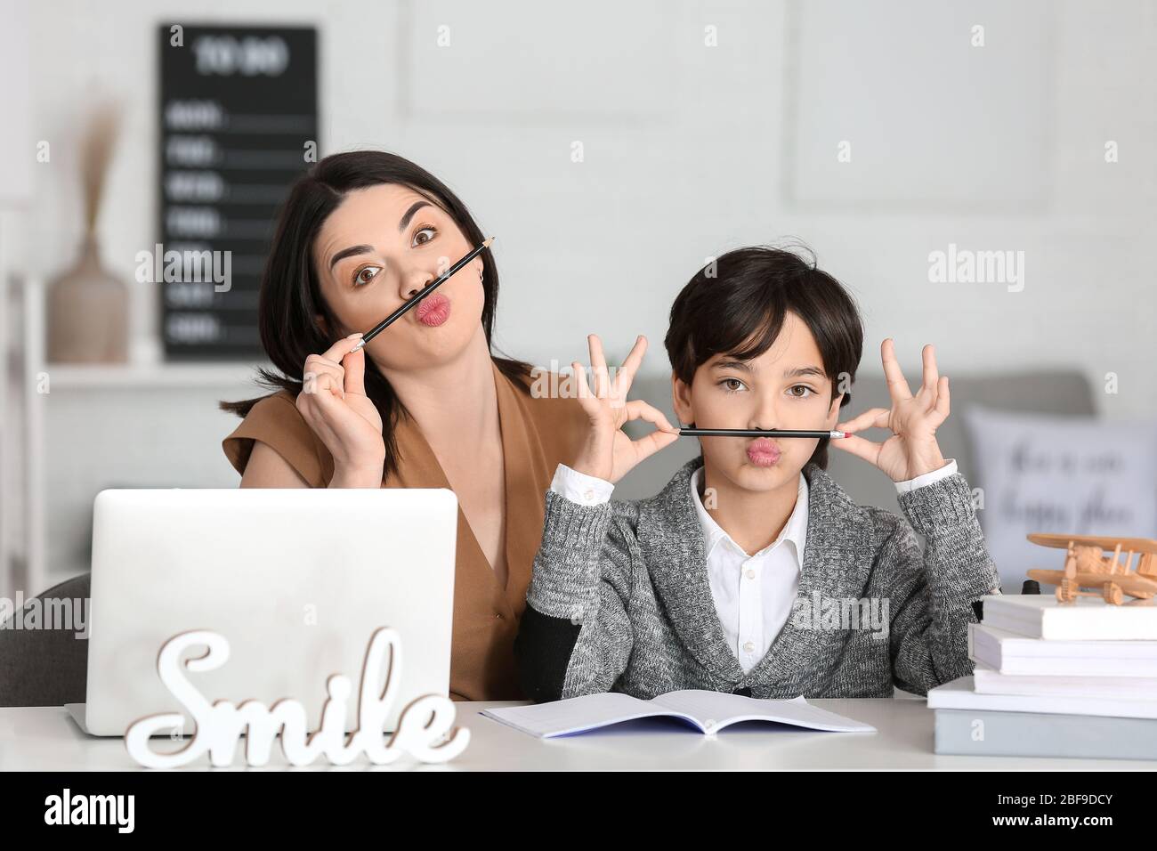 Little boy with his mother having fun while doing homework in room ...