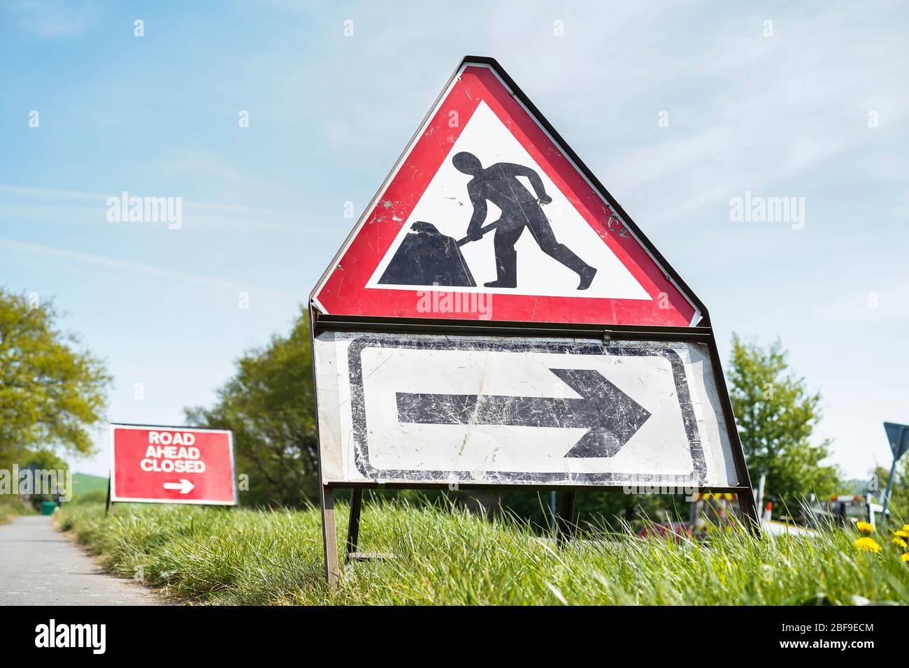 Low angle, close up triangle roadworks sign and road ahead closed sign outdoors on public UK highway on sunny spring morning. Stock Photo