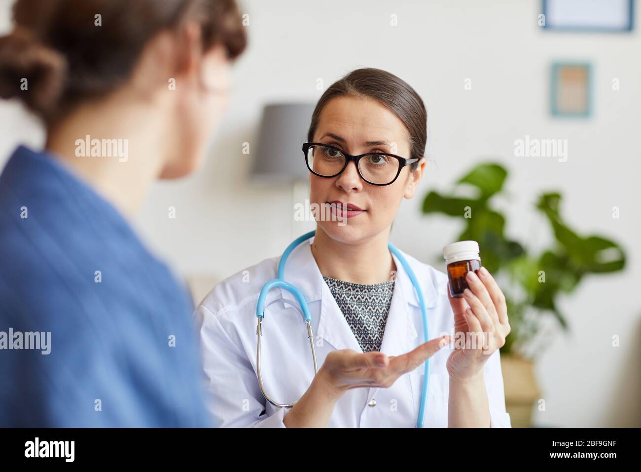 Female doctor in eyeglasses pointing at bottle with medicine in her