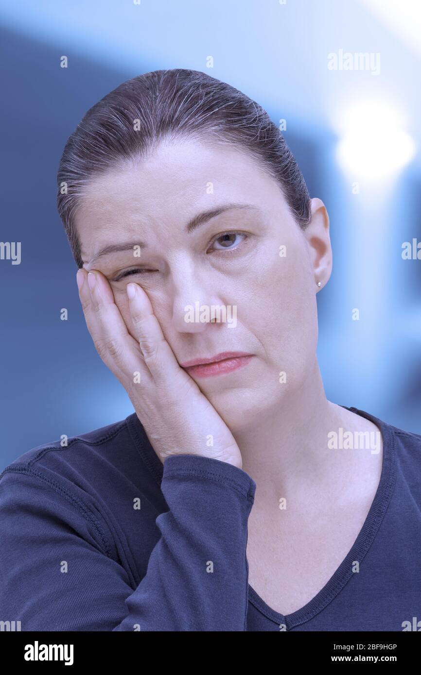 Fibromyalgia symptom fatigue: very tired woman nearly falling asleep in the office, blue filter effect Stock Photo