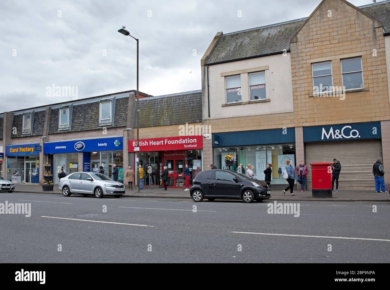 Musselburgh, High Street, East Lothian, Scotland, UK. Very quiet pavements due to the Coronavirus Lockdown but several cars passing through. The busiest area for pedestrians was outside Boots Pharmacy, (The Chemist) Pictured, where people were social distancing in the queue. Stock Photo