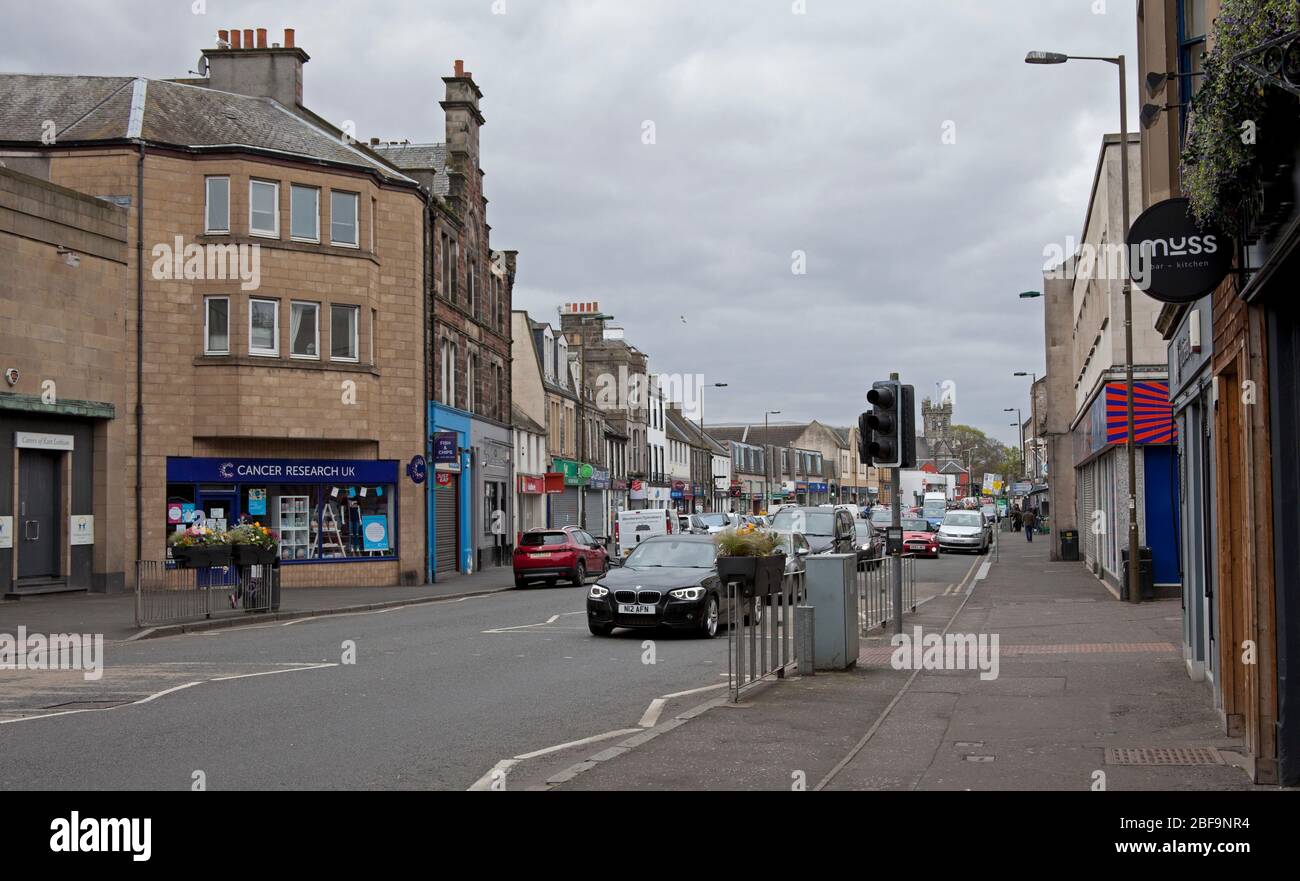 Musselburgh, High Street, East Lothian, Scotland, UK. The normally bustling main street in normal times shows very quiet pavements due to the Coronavirus Lockdown but several cars passing through. The busiest area for pedestrians was outside Boots The Chemist where people were social distancing in the queue. Stock Photo