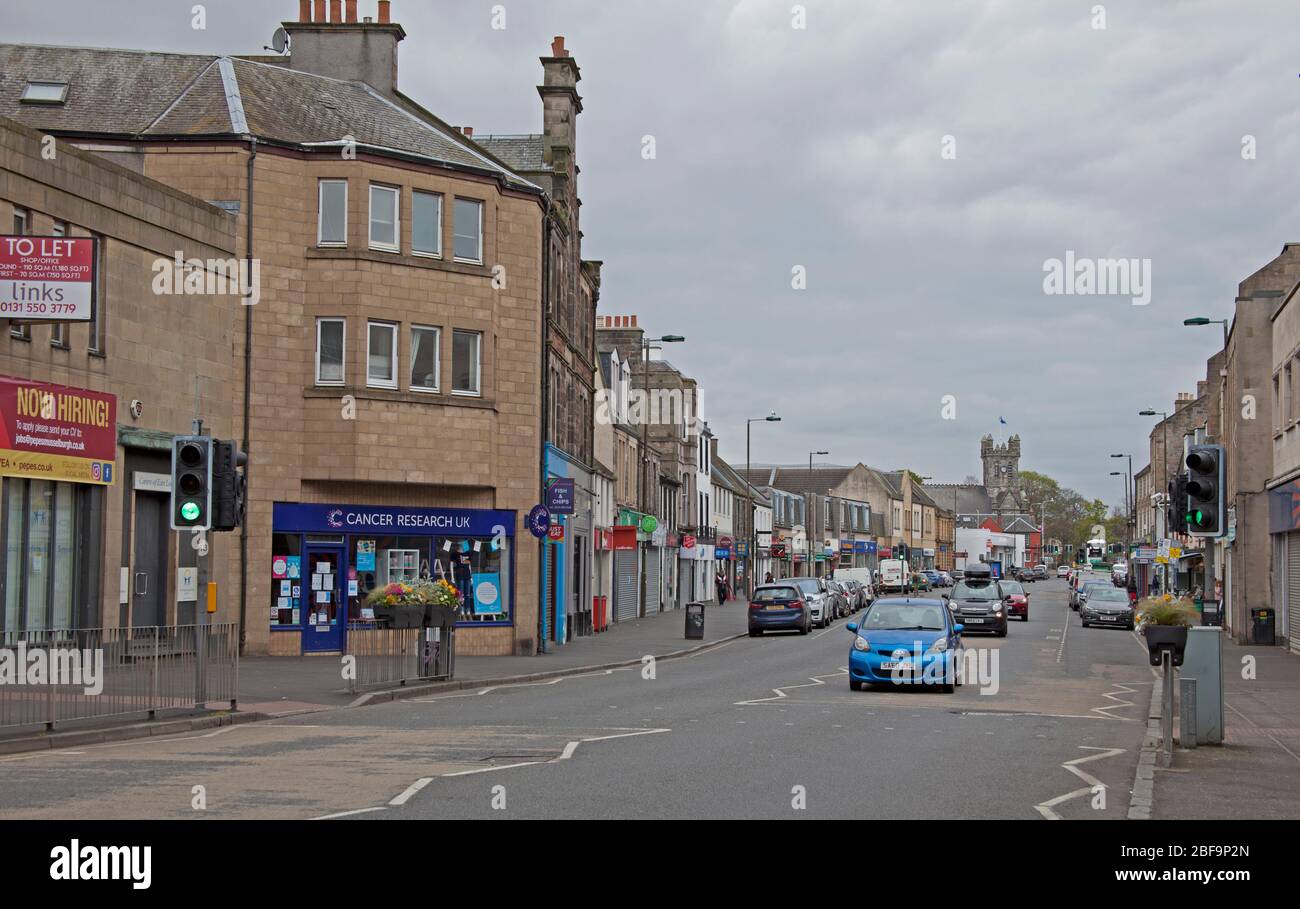 Musselburgh, High Street, East Lothian, Scotland, UK. The normally bustling main street in normal times shows very quiet pavements due to the Coronavirus Lockdown but several cars passing through. Stock Photo