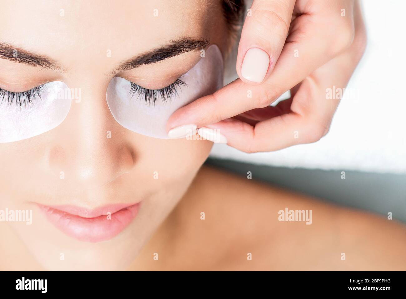 Cosmetologist hand glue duct tape under eyes of young woman before ...